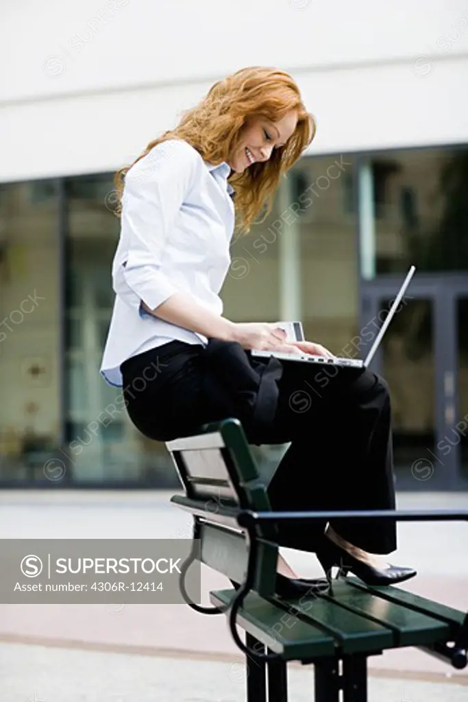Woman sitting on a bench using her laptop, Stockholm, Sweden.