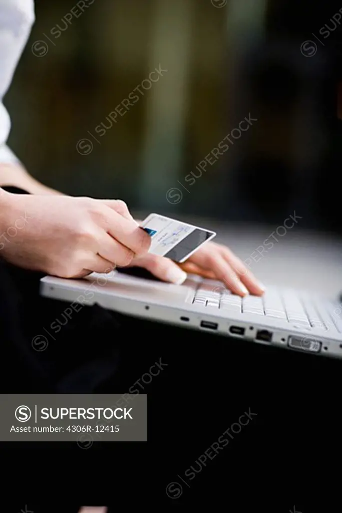 Pair of hands, a credit card in one hand and the other hand on a laptop, Stockholm, Sweden.