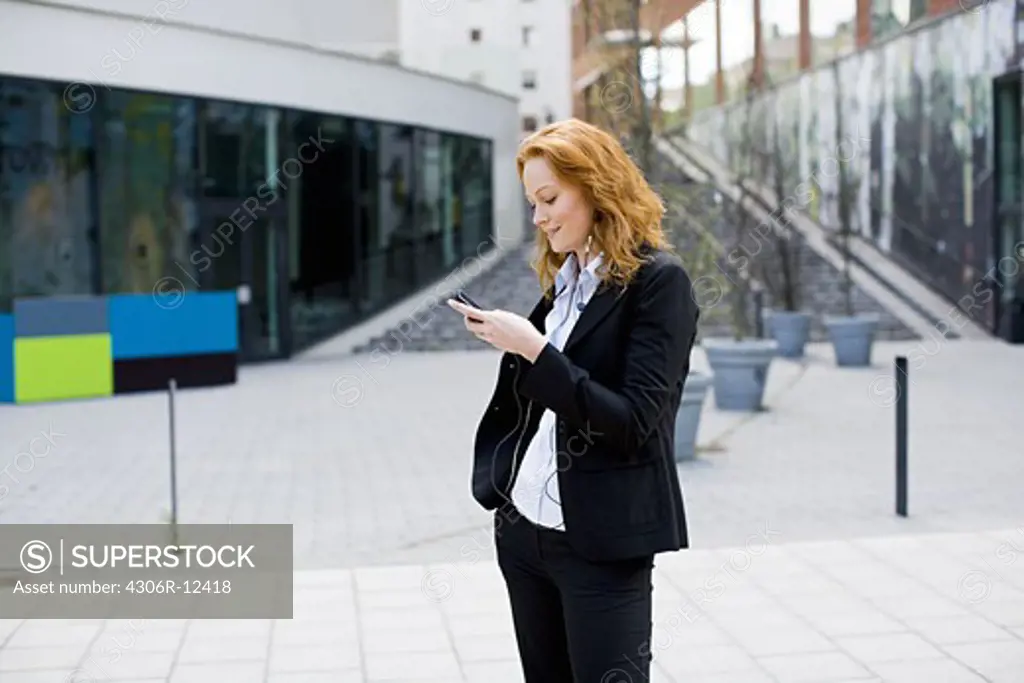 Woman standing outdoors with a cellphone and headset, Stockholm, Sweden.
