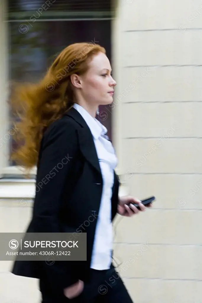 Woman walking fast holding her cellphone, Stockholm, Sweden.