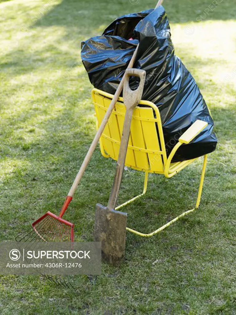 A yellow chair, a black bin bag and garden tools, Sweden.