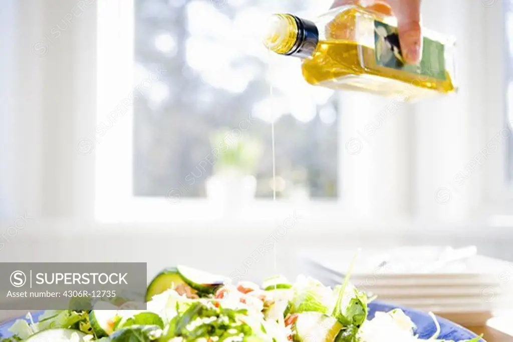 A peson pouring olive oil on a salad, Sweden.