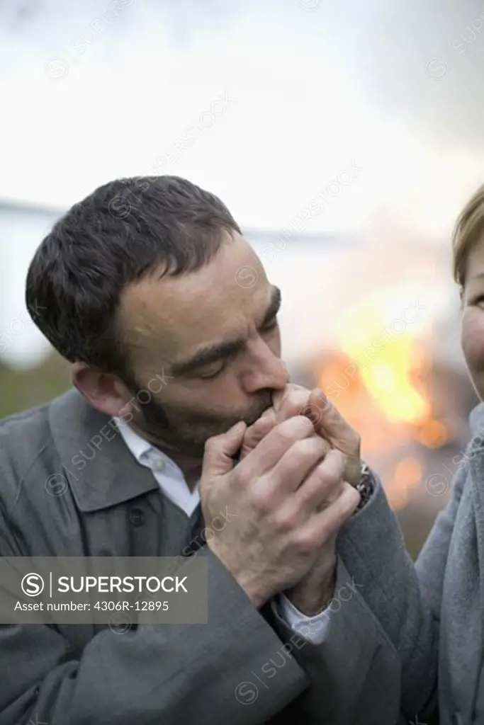 A man kissing the hand of a woman in front of a bonfire, Sweden.