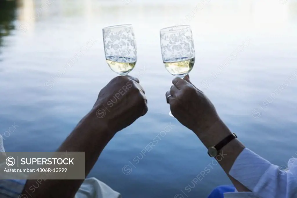 The hands of a senior couple toasting on a jetty, Sweden.