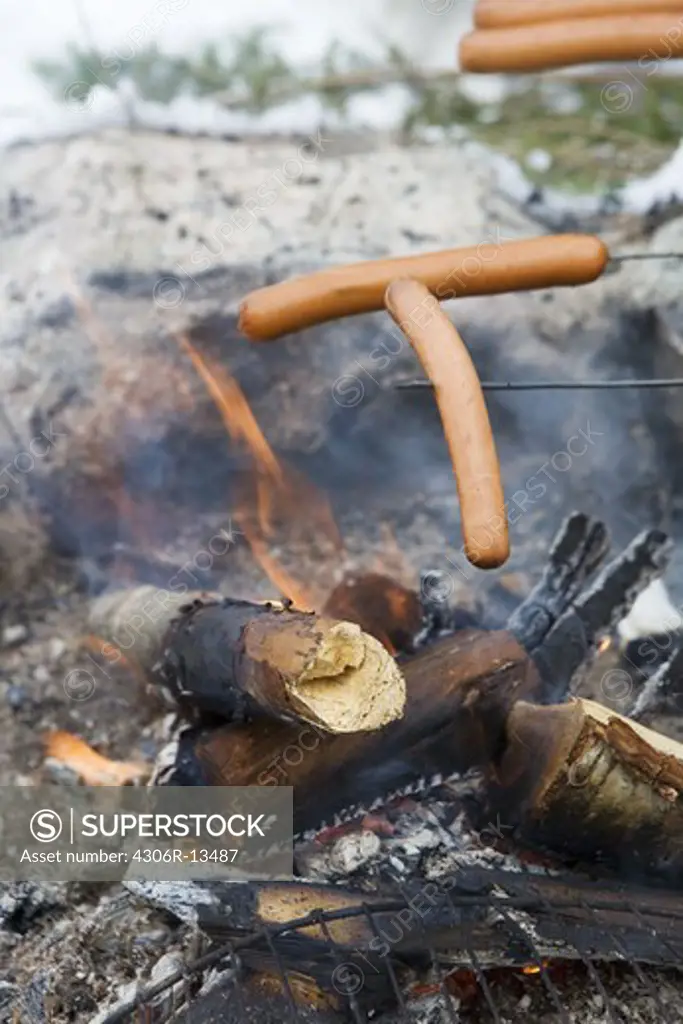 Sausages being grilled over camp fire, Sweden.