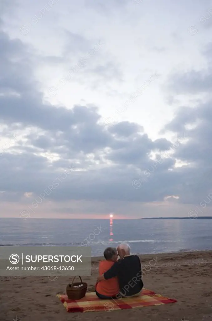 An elderly couple sitting on a beach, Skane, Sweden.