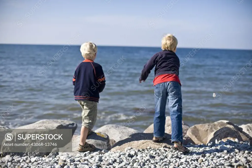 Two boys throwing stones into the water, Gotland, Sweden.