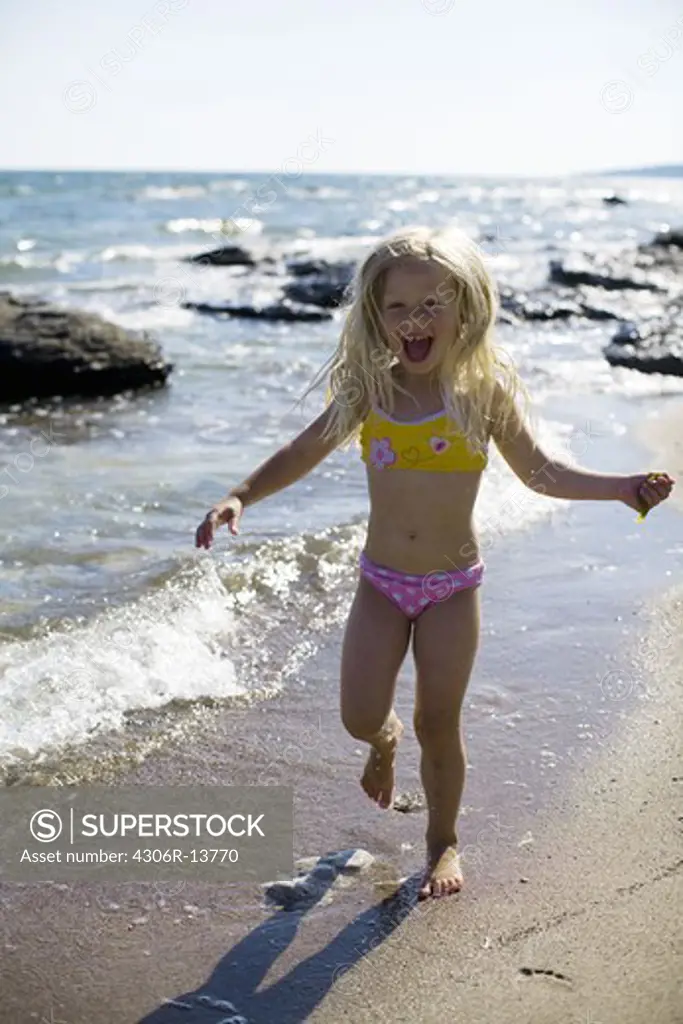 A smiling girl running at the water''s edge, Gotland, Sweden.
