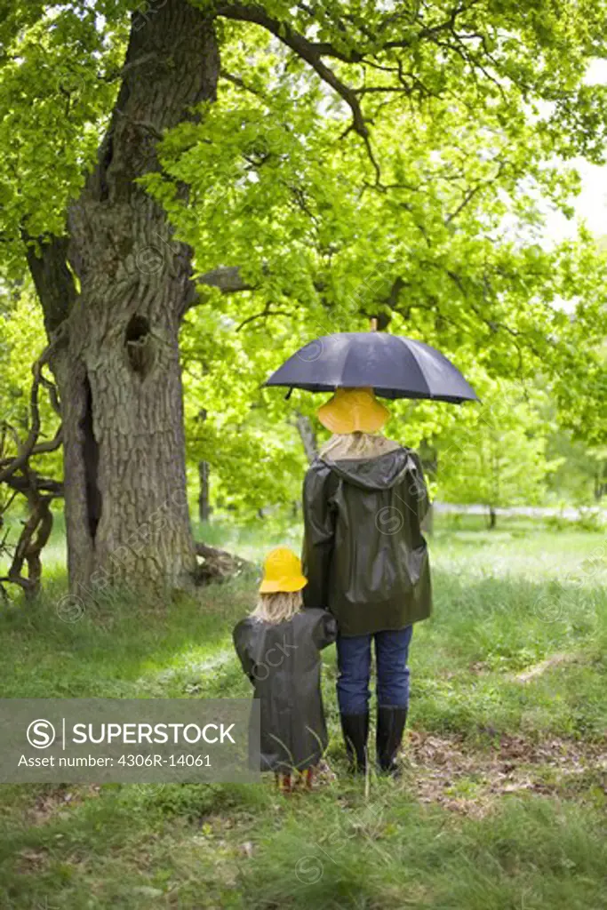 Mother and daughter walking in the rain in a park, Sweden.