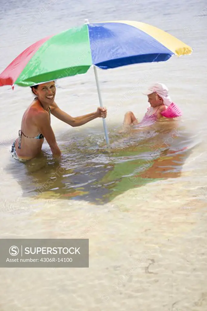 Mother and daughter under a parasol in the sea, Greece.