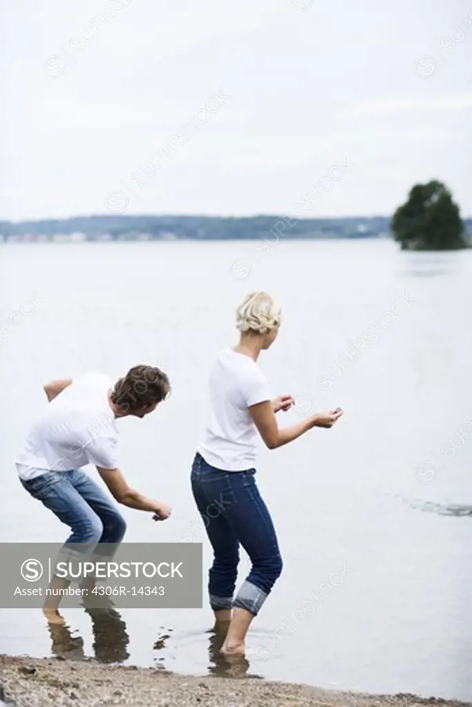 A man and a woman throwing pebbles trying to make them bounce on the surface of the water, Sweden.
