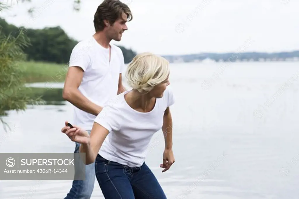 A man and a woman throwing pebbles trying to make them bounce on the surface of the water, Sweden.