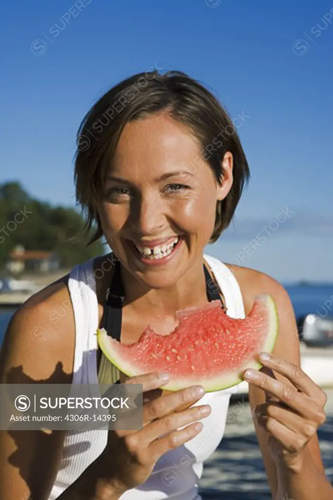 A woman eating a watermelon by the sea in the archipelago of Stockholm, Sweden.