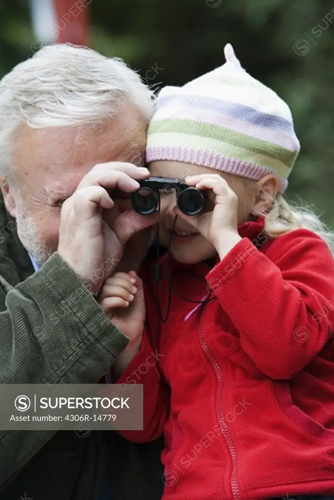 Grandfather and grandchild looking through binoculars, Sweden.