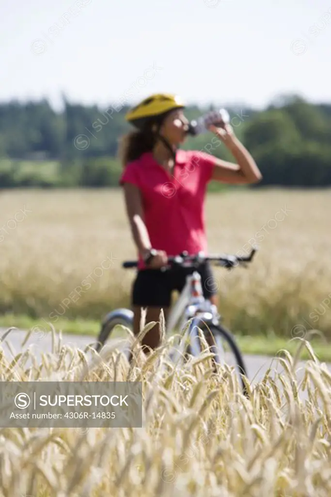 A woman riding a bike and drinking water in the countryside, Sweden.
