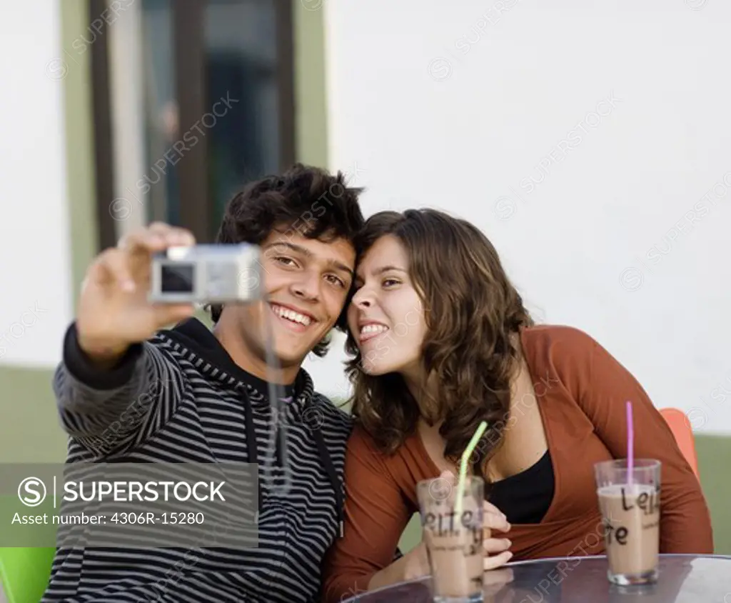 A young couple sitting at a cafe holding a camera, Portugal.