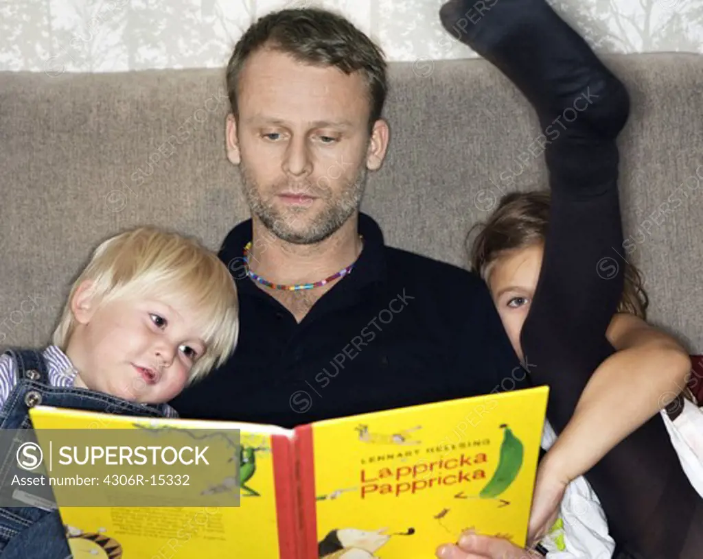Father, son and daughter reading a book together, Sweden.