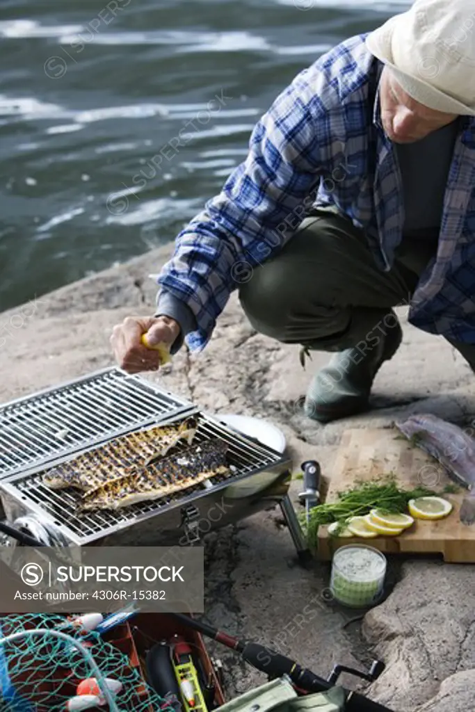 A man barbecuing fish by the water, Sweden.