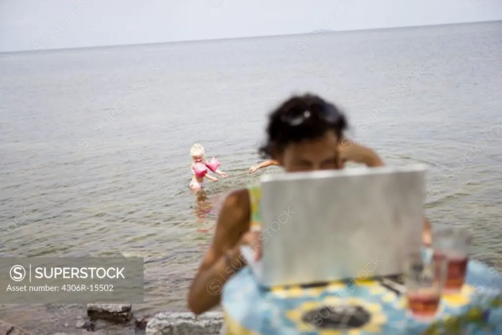 Woman using a laptop on the beach, Oland, Sweden.