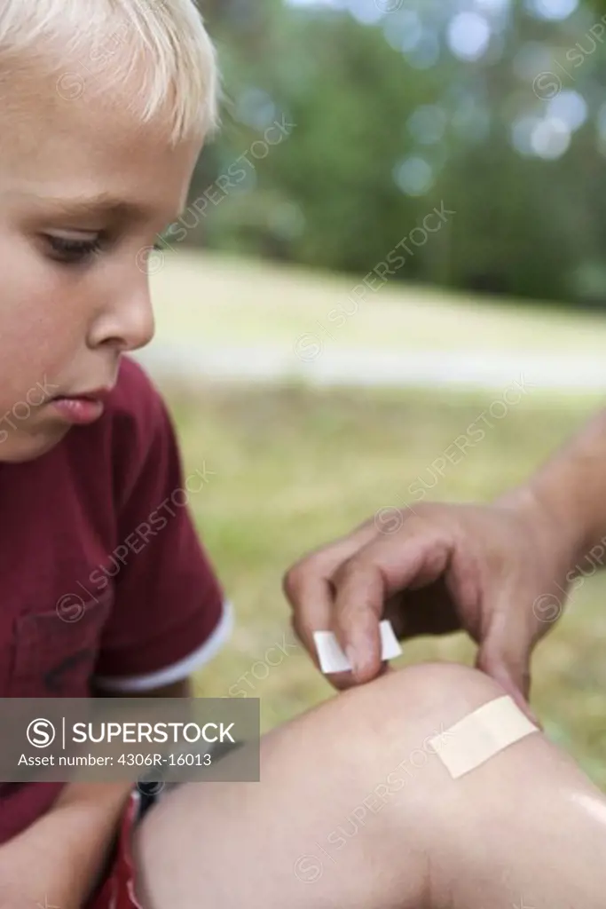 A father putting on a plaster on the knee of his son, Sweden.