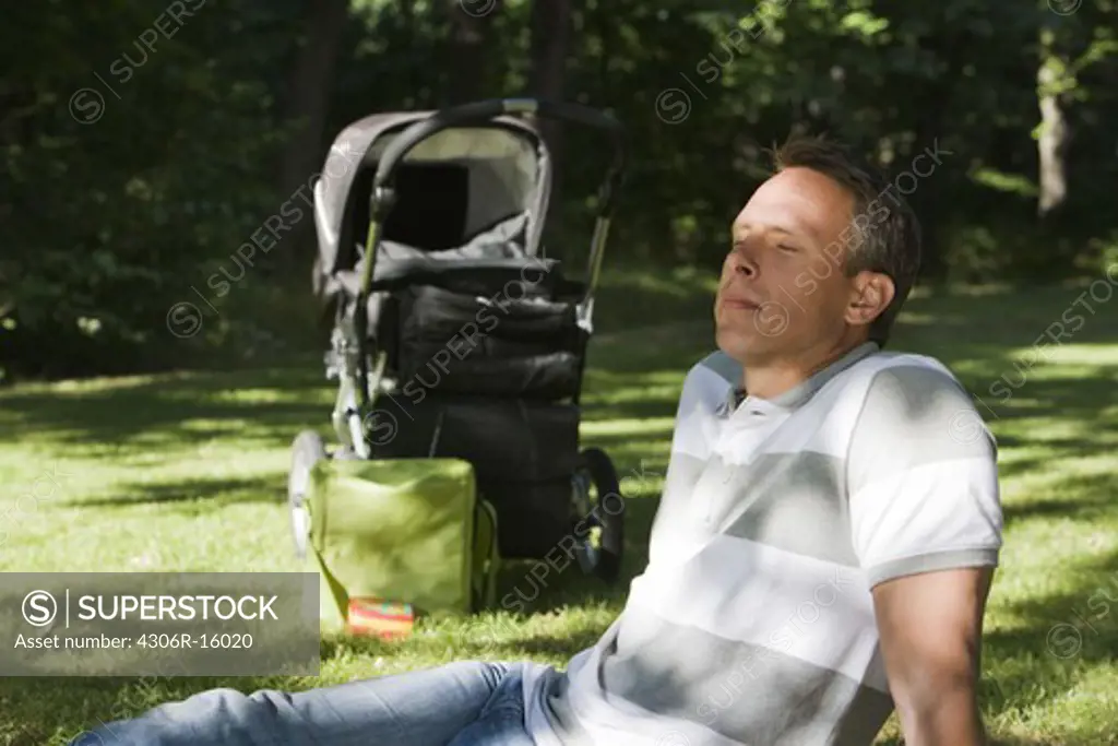 A man with a pram and a computer in a park a sunny day, Sweden.