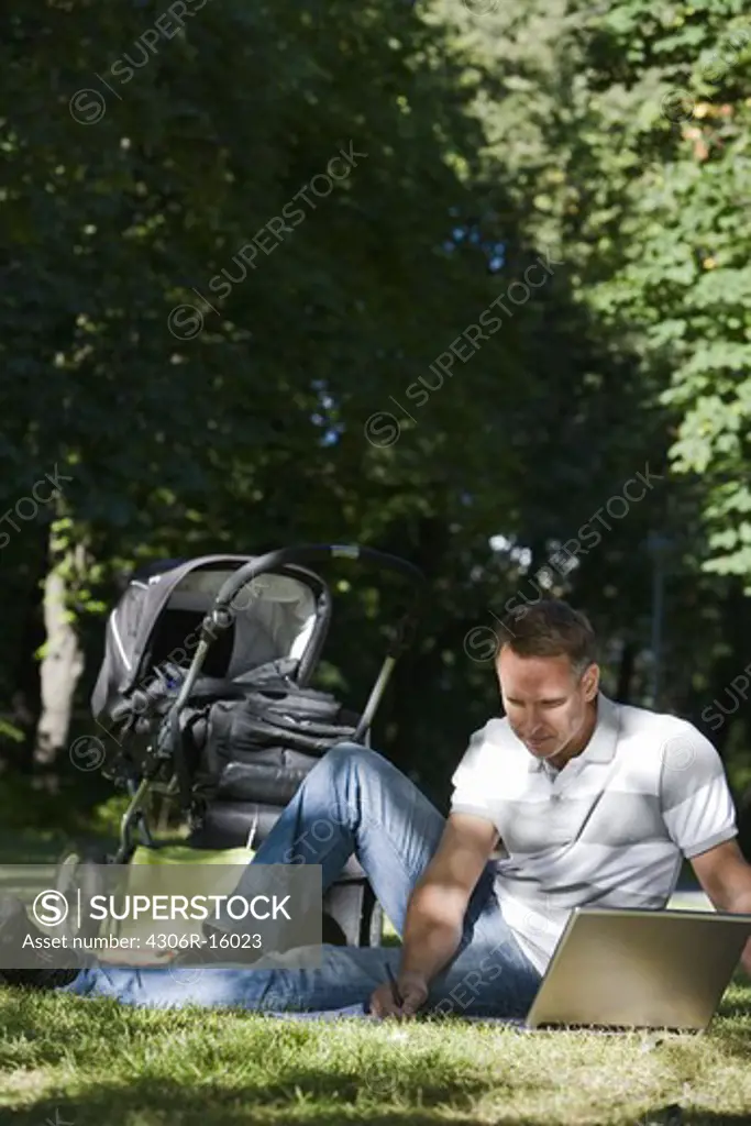 A man with a pram and a computer in a park a sunny day, Sweden.