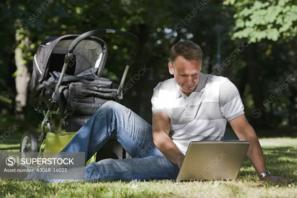 A man with a pram and a computer in a park a sunny day, Sweden.