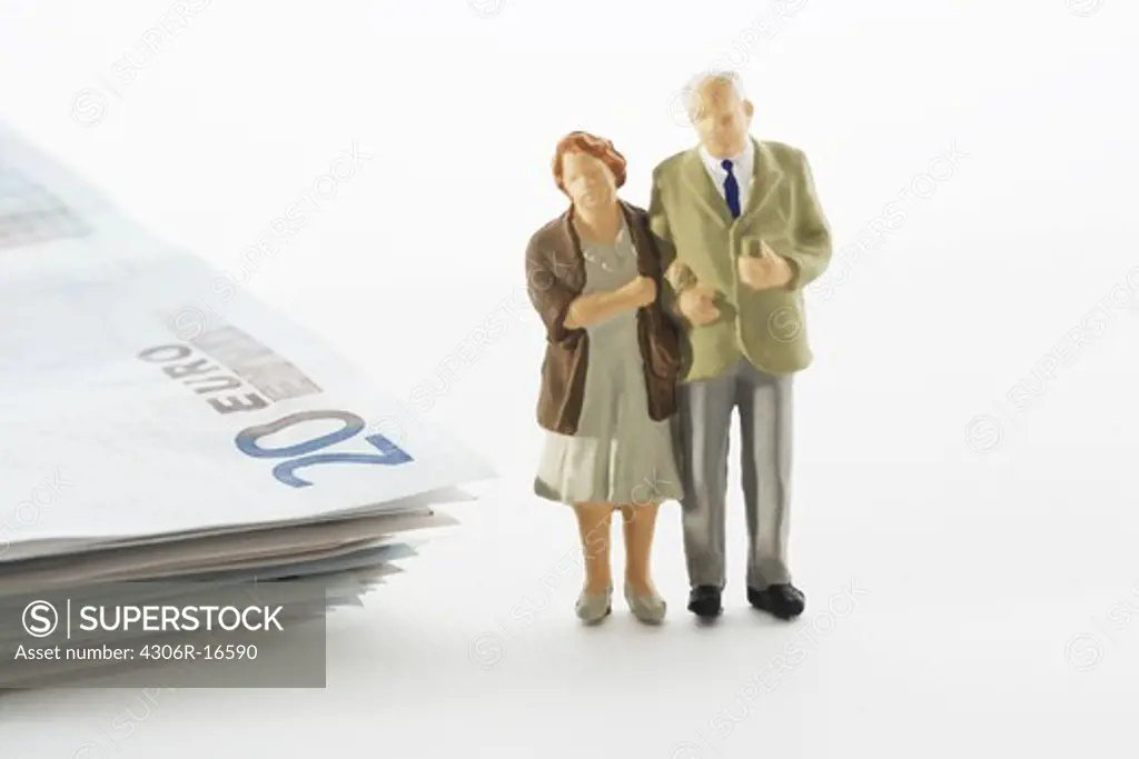 Figures in the shape of a senior couple standing next to a bundle of notes.