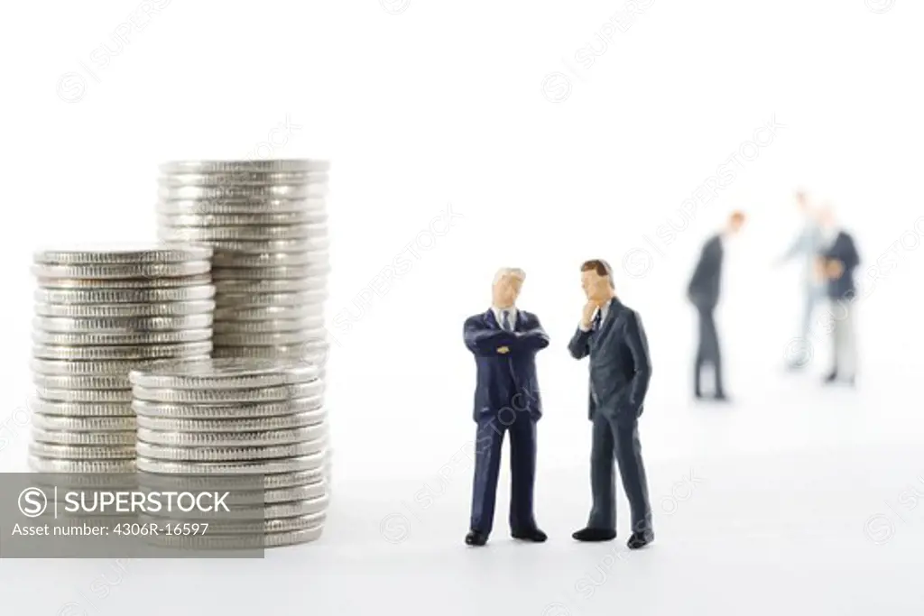 Figures in the shape of business men standing next to a pile of coins.
