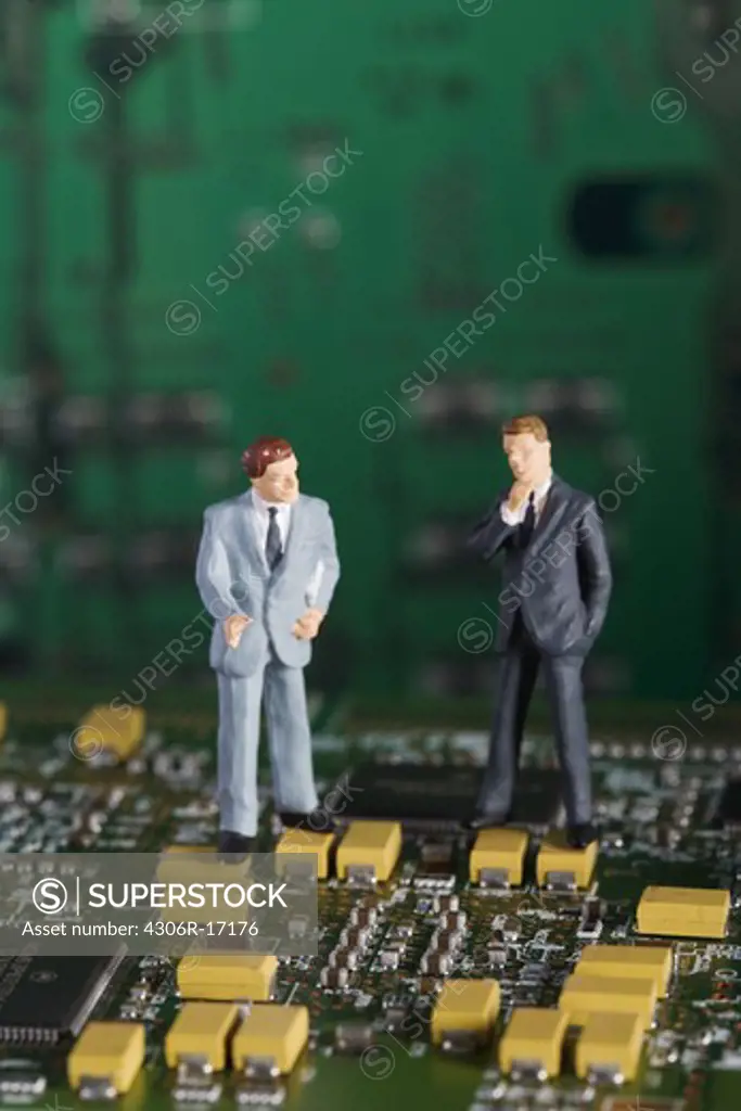 Figures in the shape of business men standing in a printed circuit card.