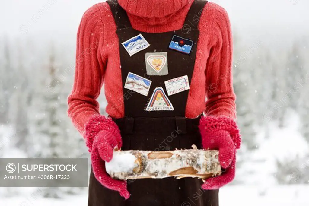 A woman wearing ski clothing holding a log  of wood, Sweden.