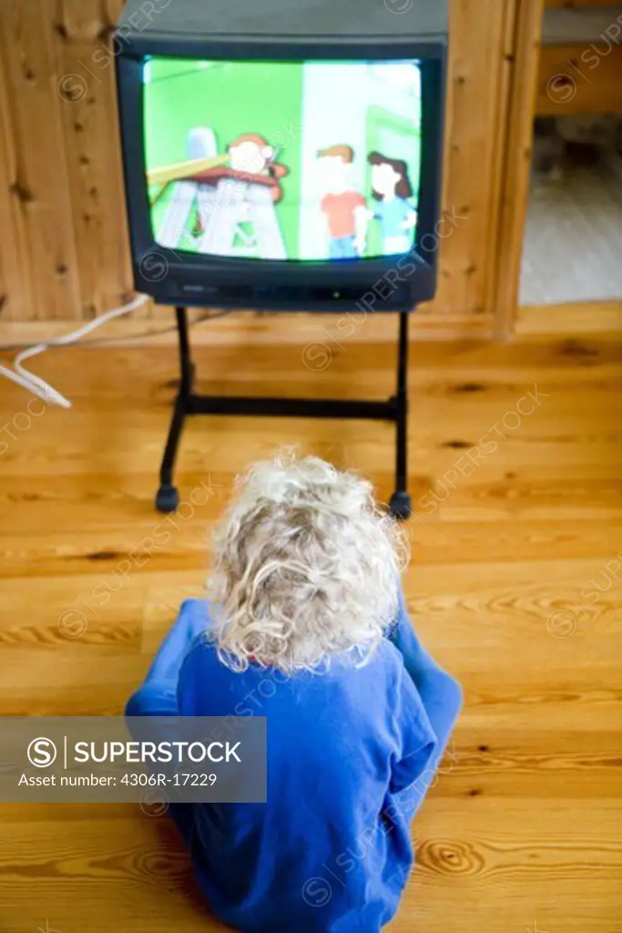 A girl sitting on the floor watching TV.