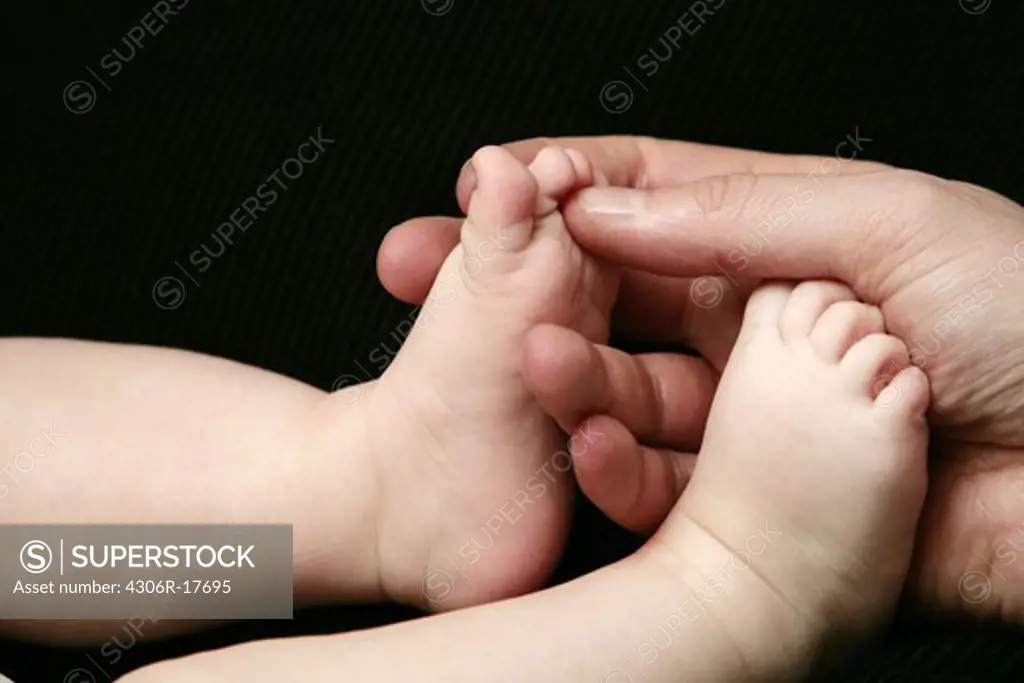 An adult hand and baby feet, close-up.
