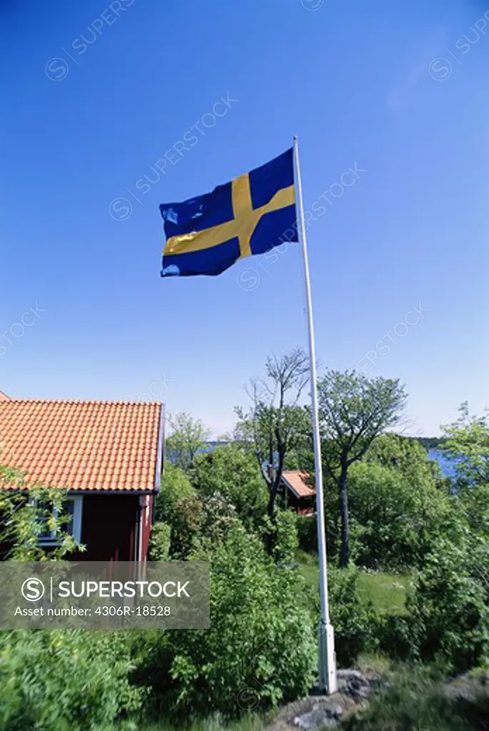 The Swedish flag and a red cottage by the water, Sweden.