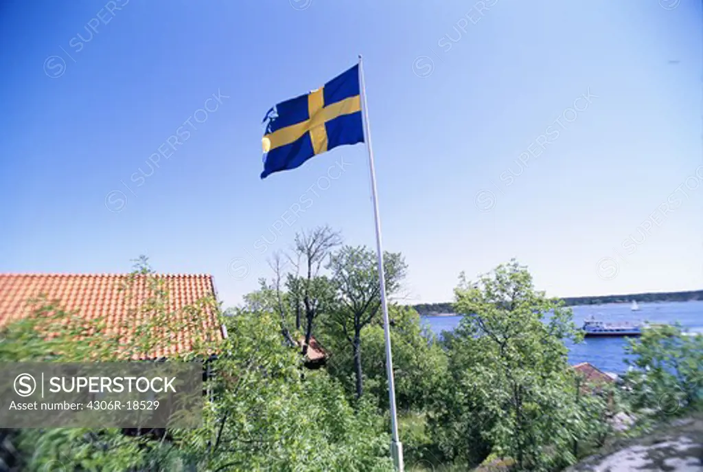 The Swedish flag and a red cottage by the water, Sweden.