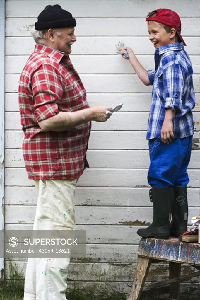 Grandfather and grandson painting their summer cottage, Sweden.