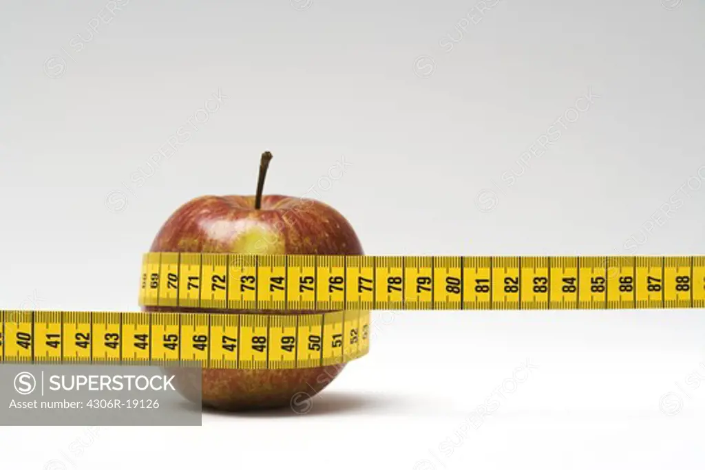 An measuring-tape around an apple, close-up.