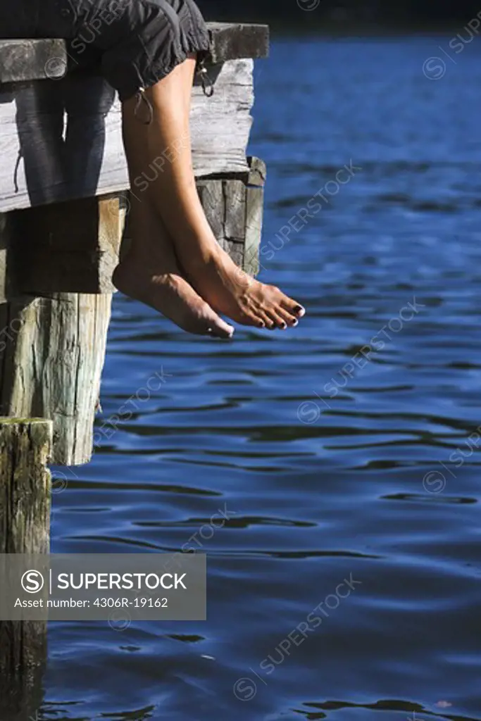 The legs of a woman sitting on a jetty by a lake, Sweden.