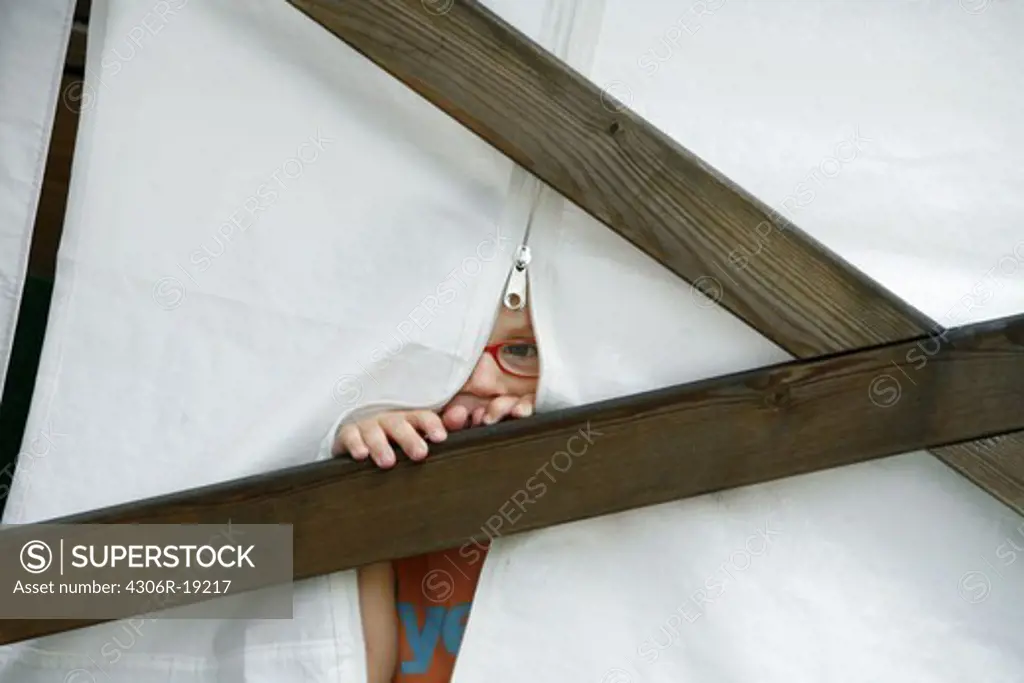 A little boy looking through a hole in a tent.
