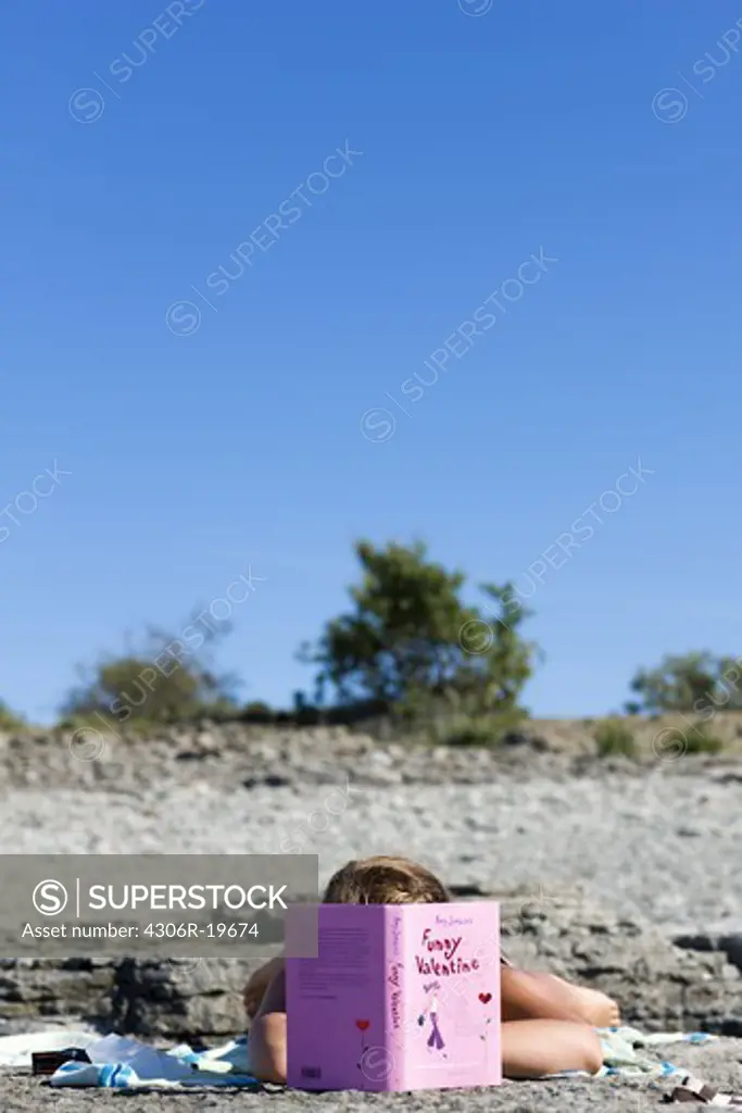 A teenage girl reading on the beach, Sweden.