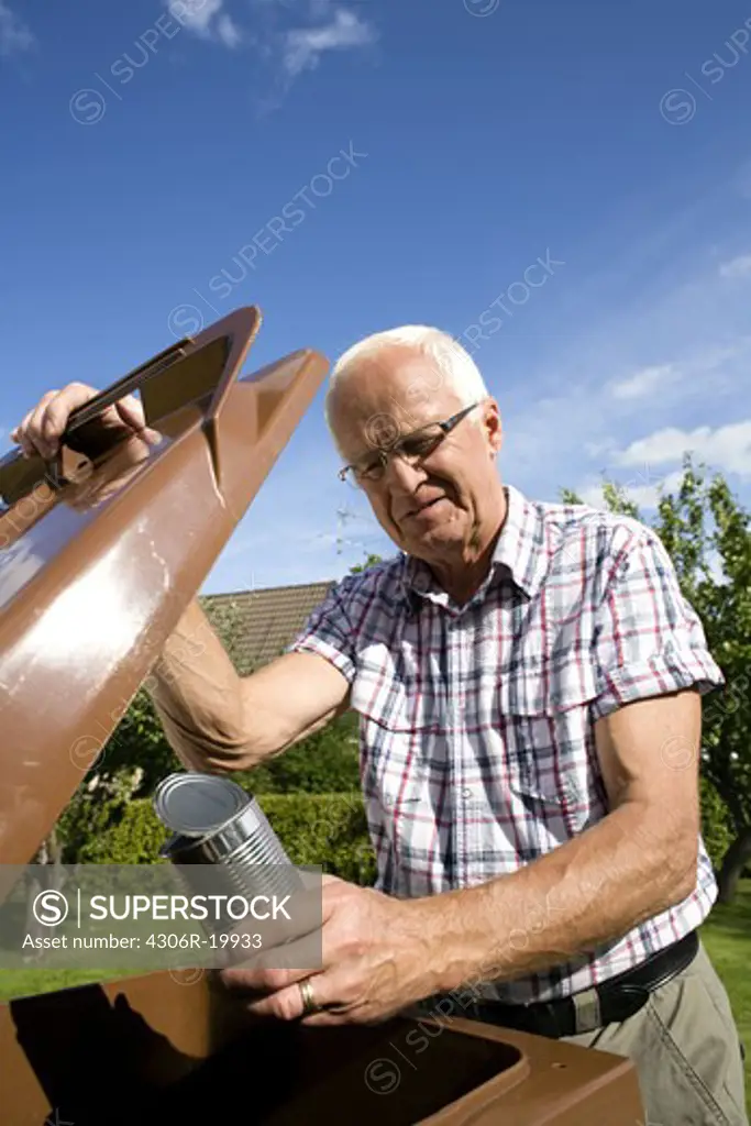 An elderly man holding a tin by a dustbin, Sweden.