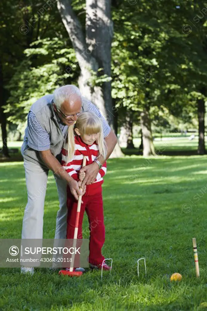 Girl and senior man playing croquet in the park, Sweden.