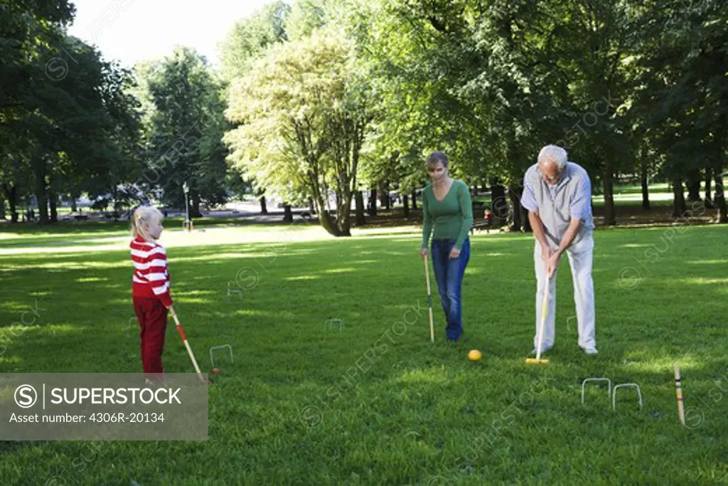 Senior man, girl and woman playing croquet in the park, Sweden.