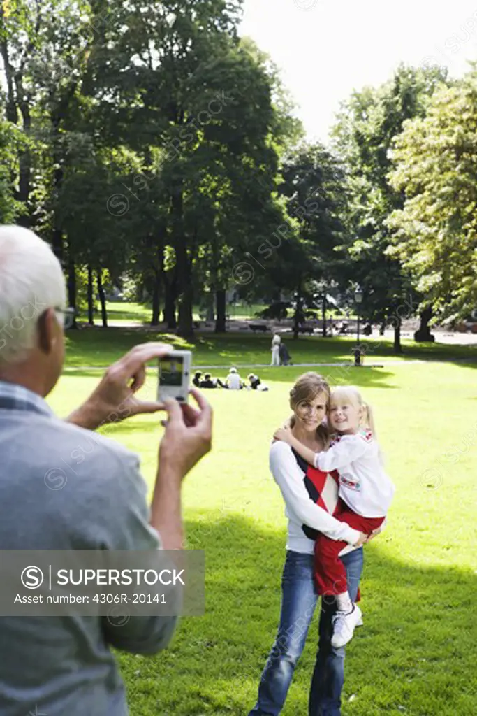 Woman, senior man and girl taking photographs in the park, Sweden.