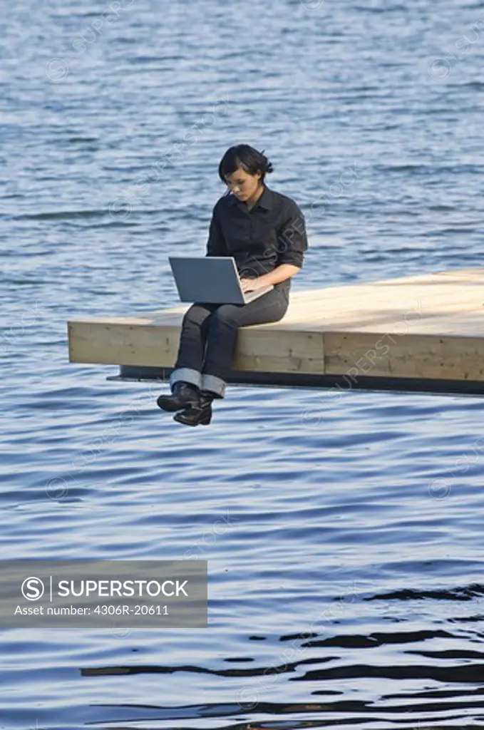 Young woman on a jetty using a laptop, Sweden.