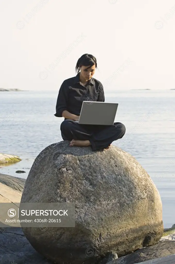 A young woman on a rock using a laptop, Sweden.