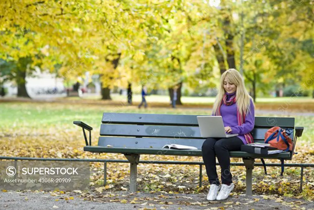 A woman sitting on bench in a park using a laptop, Stockholm, Sweden.