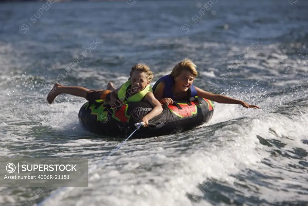 Boys riding on a plastic object drawn by a motorboat, Sweden.