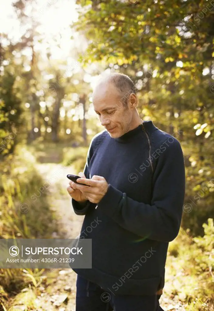Man in the forest looking at his mobile phone, Sweden.