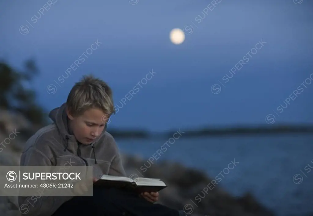 A boy reading a book in the moonlight, Sweden.